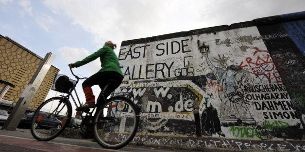 A woman cycles past a portion of the Berlin Wall on October 16, 2008 at the East Side Gallery in Berlin. The East Side Gallery, a more than one kilometre long section of the Wall decorated with paintings by international artists, is to be restored, as most of the paintings are badly damaged by erosion, graffiti and vandalism. AFP PHOTO BARBARA SAX (Photo credit should read BARBARA SAX/AFP/Getty Images)