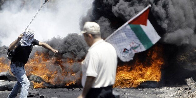 A Palestinian protester (L) hurls rocks at Israeli security forces as man walks past with a Palestinian flag during clashes f