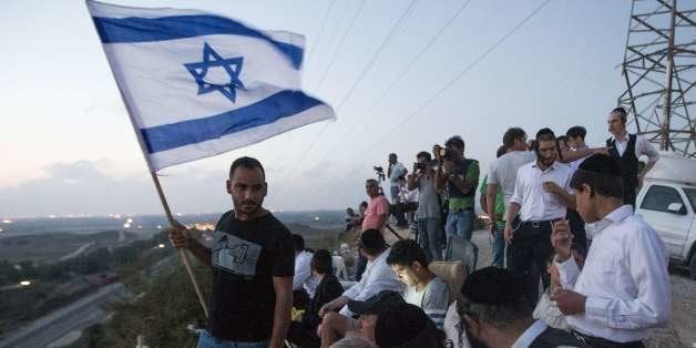 Israelis, mostly residents of the southern Israeli city of Sderot, stand with an Israeli flag on a hill overlooking the Gaza