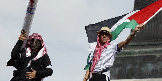 A protester wearing a gas mask and a kaffiyeh holds a fake rocket with the Israeli flag, swastikas and a nuclear symbol next to another waving a Palestinian flag on July 13, 2014 in Paris, during a demonstration against Israel and in support of residents in the Gaza Strip, where a six-day conflict has left 166 Palestinians dead. Clashes erupted on Bastille Square at the end of the march attended by thousands, with people throwing objects onto a cordon of police who responded with tear gas. The unrest was continuing early in the evening. AFP PHOTO / KENZO TRIBOUILLARD (Photo credit should read KENZO TRIBOUILLARD/AFP/Getty Images)