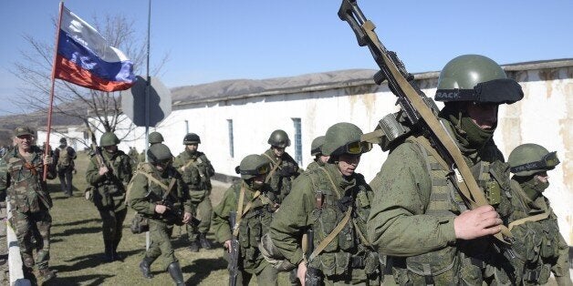 A man with a Russian flag greets armed men in military fatigues blocking access to a Ukrainian border guards base not far fro