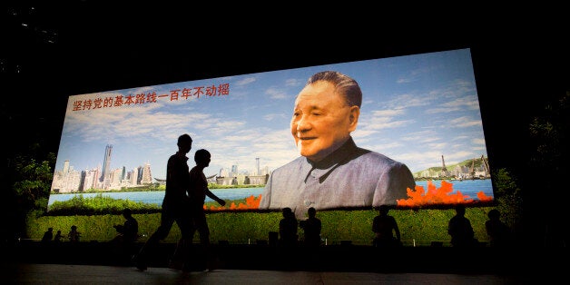 People walk past a portrait of China's former leader Deng Xiaoping that reads 'Persist with the Communist Partys fundamental