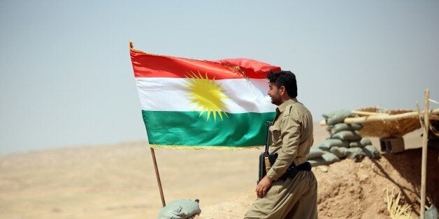A peshmerga fighter stands next to a Kurdish flag as he guards a position near the strategic Jalawla area, in Diyala province