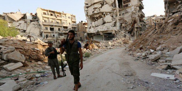 Rebel fighters walk in front of damaged buildings in Karam al-Jabal neighbourhood of Aleppo on August 26, 2014. The United States has begun reconnaissance flights over Syria and is sharing intelligence about jihadist deployments with Damascus through Iraqi and Russian channels, sources told AFP. AFP PHOTO/AMC/ZEIN RIFAI (Photo credit should read ZEIN AL-RIFAI/AFP/Getty Images)