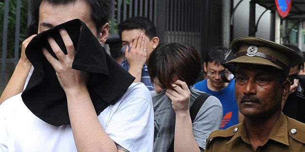 Arrested Chinese nationals are escorted by Sri Lankan police as they are taken to a remand prison after being produced before the magistrate court in Colombo on December 22, 2012. Police in Sri Lanka on Saturday said had arrested 100 Chinese nationals for currency fraud in a string of raids in and around the capital Colombo in what they described as a case of cyber-crime. AFP PHOTO/ LAKRUWAN WANNIARACHCHI (Photo credit should read LAKRUWAN WANNIARACHCHI/AFP/Getty Images)