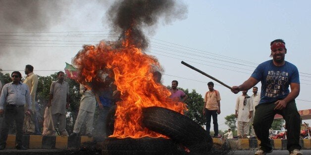 LAHORE, PAKISTAN - AUGUST 31: A supporter of the Pakistan Tehreek-e-Insaf (PTI) political party burns a tyre as they block the road with burning tires in Lahore, Pakistan on August 31, 2014. At least 4 people killed and more than 500 wounded in clashes between thousands of police and protesters in Pakistan's capital Islamabad Saturday, as a fortnight-long political impasse took a violent turn when opposition groups attempted to storm the prime minister's residence. (Photo by Rana Irfan Ali/Anadolu Agency/Getty Images)