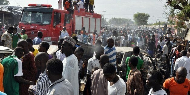 People gather near burnt vehicles as other stand on a fire truck at the site of a bomb explosion that rocked the busiest roundabout near the crowded Monday Market in Maiduguri, Borno State, on July 1, 2014. A truck exploded in a huge fireball killing at least 15 people on July 1 in the northeast Nigerian city of Maiduguri, the latest attack in a city repeatedly hit by Boko Haram Islamists. AFP PHOTO/STRINGER (Photo credit should read STRINGER/AFP/Getty Images)