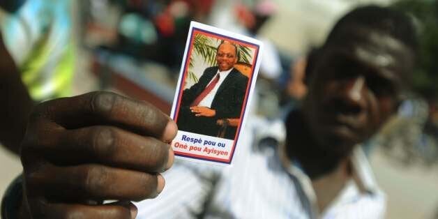 A man holds a picture of former President of Haiti, Jean-Bertrand Aristide during a rally to conmemorate the 10th anniversary of his second ouster, in Port-au-Prince, on February 27, 2014. AFP PHOTO/Hector RETAMAL (Photo credit should read HECTOR RETAMAL/AFP/Getty Images)