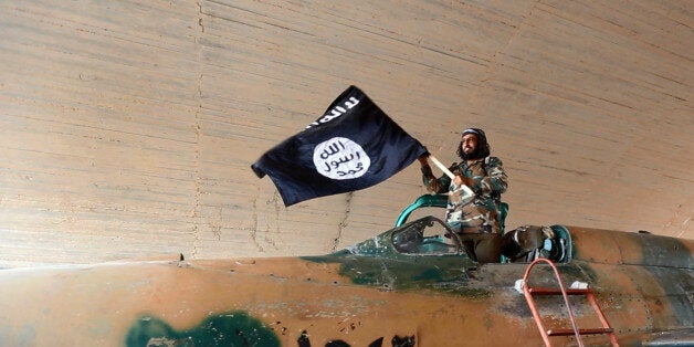 This undated image posted on Wednesday, Aug. 27, 2014 by the Raqqa Media Center of the Islamic State group, a Syrian opposition group, which has been verified and is consistent with other AP reporting, shows a fighter of the Islamic State group waving their flag from inside a captured government fighter jet following the battle for the Tabqa air base, in Raqqa, Syria on Sunday. A U.N. commission on Wednesday accused the extremist Islamic State organization of committing crimes against humanity with attacks on civilians, as pictures emerged of the extremists' bloody takeover of a Syrian military air base that added to the international organizationâs claims. (AP Photo/ Raqqa Media Center of the Islamic State group)