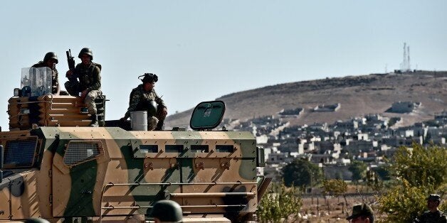 Turkish soldiers stand in front of the Syrian town of Ain al-Arab, known as Kobane by the Kurds, at the Mursitpinar border crossing on the Turkish-Syrian border in the southeastern town of Suruc, Sanliurfa province, on October 5, 2014. A mortar that crashed into a house on Turkish territory just a few kilometres from a border area inside Syria where Kurdish fighters are battling Islamic State (IS) jihadists wounded five people on October 5, medical sources said. Mortars have on occasion hit Turkish territory over the last days amid the fighting for the Syrian town of Kobane, leaving several people wounded. Turkish forces are deployed on the border but not taking part in the fighting. AFP PHOTO / ARIS MESSINIS (Photo credit should read ARIS MESSINIS/AFP/Getty Images)