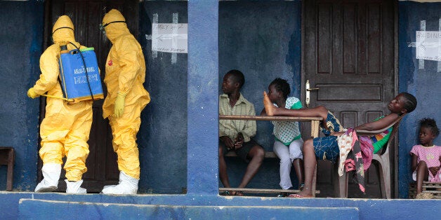 FILE - In this Tuesday Sept. 30, 2014 file photo, residents of the village of Freeman Reserve, about 30 miles north of Monrovia, Liberia, watch members of District 13 ambulance service disinfect a room as they pick up six suspected Ebola sufferers that had been quarantined. Six months into the worldâs worst-ever Ebola outbreak, and the first to happen in an unprepared West Africa, the gap between what has been sent by other countries and private groups and what is desperately needed is huge. Even as countries try to marshal more resources to close the gap, those needs threaten to become much greater, and possibly even insurmountable. (AP Photo/Jerome Delay, File)