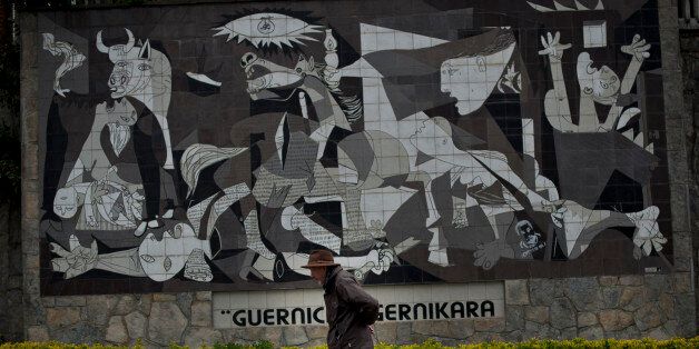 A man walks past a wall with a reproduction of Pablo Picasso's "Guernica" painting, during a tribute to people who died in Guernica, northern Spain, on the 77th anniversary of the attack, Saturday April 26, 2014. The small Basque town was raided in a German bomber attack and some thousands of Basque citizens lost their lives on this day in 1937. The carnage has since stood as a symbol of man's cruelty to his fellow man, immortalized in Pablo Picasso's immense and powerful painting, "Guernica". (AP Photo/Alvaro Barrientos)
