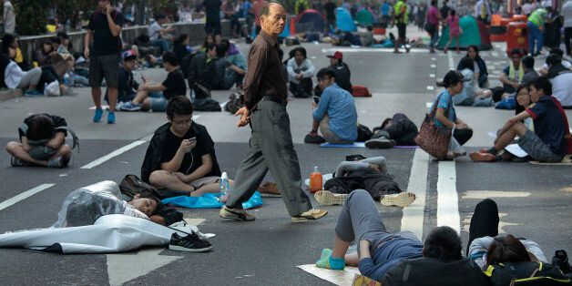 A man walks among dozens of sleeping student protesters in the Mong Kok district of Hong Kong, Saturday, Oct. 18, 2014. Hong Kong riot police battled with thousands of pro-democracy protesters for control of the city's streets Friday night, using pepper spray and batons to hold back defiant activists who returned to a protest zone that officers had partially cleared. (AP Photo/Wally Santana)