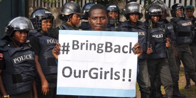 A man poses with a sign in front of police officers in riot gear during a demonstration calling on the government to rescue the kidnapped girls of the government secondary school in Chibok, in Abuja, Nigeria, Tuesday, Oct. 14, 2014. Scores of protesters marched chanting "Bring Back Our Girls" kidnapped six months ago by Boko Haram. (AP Photo/Olamikan Gbemiga)