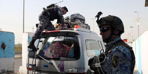 An Iraqi federal policeman stands guard as his colleague searches a car at a checkpoint in Baghdad, Iraq, Saturday, Oct. 11,