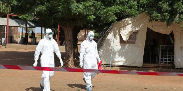 In this photo taken Saturday, Oct. 25, 2014, health workers walk towards an area used for Ebola quarantine after they worked with diseased Fanta Kone at a Ebola virus center in Kayes, Mali. After 2-year-old Fanta Koneâs father died in southern Guinea, the toddlerâs grandmother took her from the forested hills where the Ebola outbreak first began months ago to bring her home to Mali. It wasnât long, though, before the little girl started getting nosebleeds. (AP Photo/Baba Ahmed)