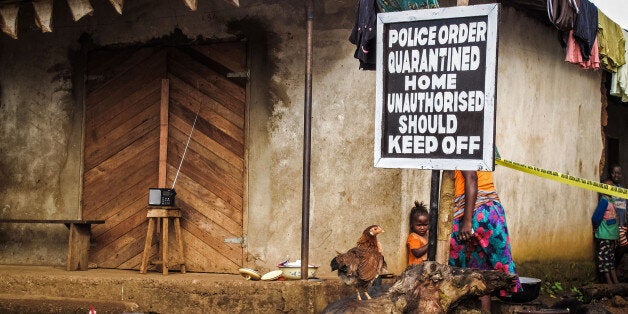 A child, center, stands underneath a signboard reading 'Police order quarantined home unauthorised should keep off' as a fami