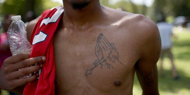 ST LOUIS, MO - AUGUST 25: A mourner at the funeral of Michael Brown displays a praying hands tattoo on his chest at St Peter's cemetery during the burial service on August 25, 2014 in St. Louis, Missouri. Michael Brown was shot and killed by a police officer in the nearby town of Ferguson, Missouri on August 9. His death caused several days of violent protests along with rioting and looting in Ferguson (Photo by Joe Raedle/Getty Images)