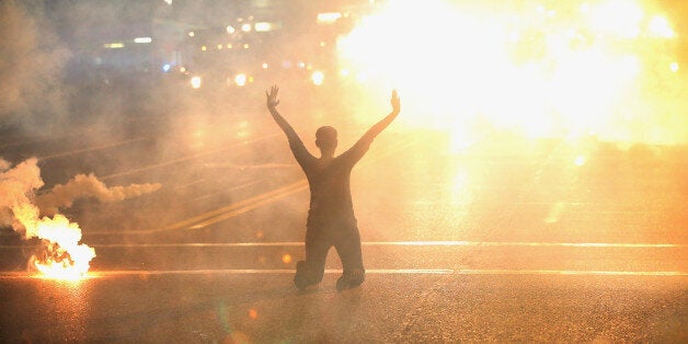 FERGUSON, MO - AUGUST 17: Tear gas reigns down on a woman kneeling in the street with her hands in the air after a demonstration over the killing of teenager Michael Brown by a Ferguson police officer on August 17, 2014 in Ferguson, Missouri. Despite the Brown family's continued call for peaceful demonstrations, violent protests have erupted nearly every night in Ferguson since his August 9, death. (Photo by Scott Olson/Getty Images)