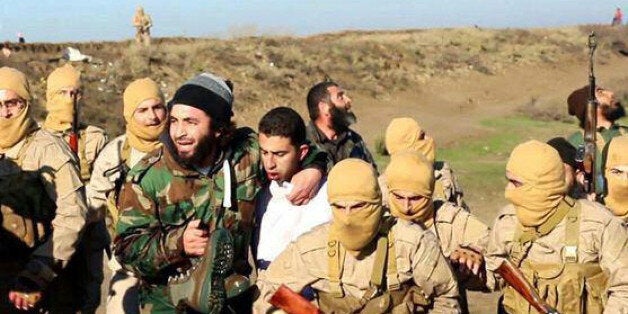 This image posted by the Raqqa Media Center of the Islamic State group, a militant extremist group, which has been authenticated based on its contents and other AP reporting, shows members of the Islamic State group while captured the pilot, center, wearing a white shirt in Raqqa, Syria, Wednesday, Dec. 24, 2014. Activists say that Islamic State fighters have shot down a warplane believed to be from the U.S.-led coalition over Syria. (AP Photo/Raqqa Media Center of the Islamic State group)