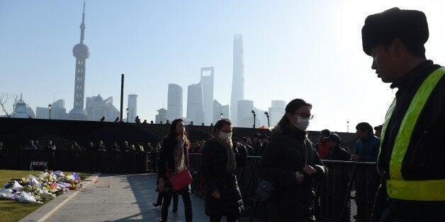 Three mourners walk past a security guard (R) after placing flowers at the site of the New Year's Eve stampede at the Bund in Shanghai on January 2, 2015. The New Year's stampede on Shanghai's historic waterfront killed at least 36 revellers, most of them women, and injured dozens more, despite efforts by authorities in China's commercial hub to mitigate the risk of overcrowding. AFP PHOTO / Greg BAKER (Photo credit should read GREG BAKER/AFP/Getty Images)