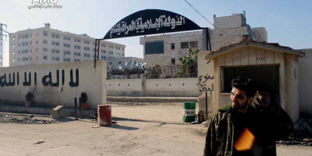 In this citizen journalism image provided by Aleppo Media Center AMC which has been authenticated based on its contents and other AP reporting, a Syrian rebel stands at the entrance to the headquarters of the Islamic State of Iraq and the Levant, after it fall to the Syrian rebels, in Aleppo, Syria, Wednesday Jan. 8, 2014. With a new label - the Islamic State of Iraq and the Levant - the global terror network al-Qaida is positioning itself as a vanguard defending a persecuted Sunni community against Shiite-dominated governments across Syria, Lebanon and Iraq. A Syrian rebellion whose aim was the removal of authoritarian president Bashar Assad is morphing into something both bigger and more ambiguous: a fight between Sunni jihadis - often foreign and animated mainly by hatred of Shiites - and almost everyone else. (AP Photo/Aleppo Media Center, AMC)