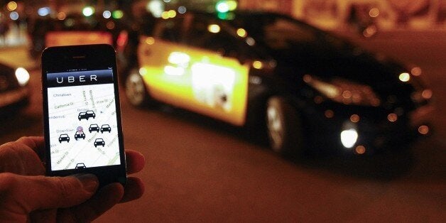 The Uber app is seen on a smartphone past cabs waiting for clients near the Sagrada Familia in Barcelona, on December 9, 2014