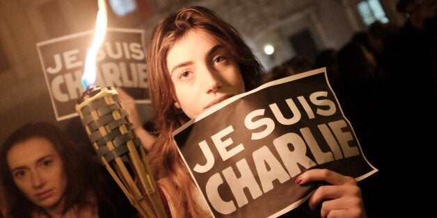 A woman holds a torch and a poster reading 'I am Charlie' in front of the French embassy on January 8, 2015 in Rome during a rally in remembrance of the victims of an attack against Charlie Hebdo satirical weekly which killed 12 people in Paris yesterday. AFP PHOTO / ALBERTO PIZZOLI (Photo credit should read ALBERTO PIZZOLI/AFP/Getty Images)