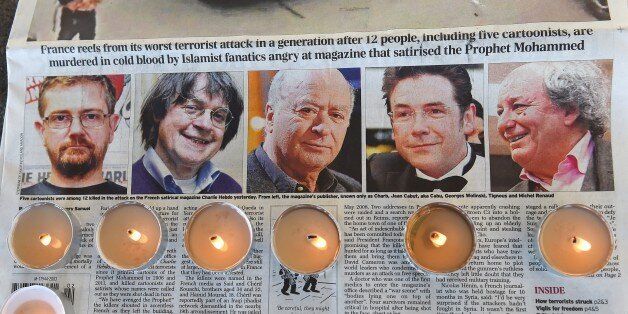 Candles are placed on a newspaper bearing pictures from (L) of French satirical weekly Charlie Hebdo's editor and cartoonists Charb, Jean Cabut, aka Cabu, Georges Wolinski and Michel Renaud who were killed the day before in an attack by two armed gunmen on the offices of French satirical newspaper Charlie Hebdo, during a gathering in Marseille, on January 8, 2015. A stunned and outraged France was in mourning yesterday, as security forces desperately hunted two brothers suspected of gunning down 12 people in an Islamist attack on a satirical weekly. AFP PHOTO / ANNE-CHRISTINE POUJOULAT (Photo credit should read ANNE-CHRISTINE POUJOULAT/AFP/Getty Images)