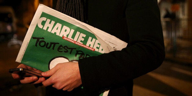 PARIS, FRANCE - JANUARY 13: A journalist holds an early copy of a Charlie Hebdo magazine while delivering a news report outside the offices of Liberation Newspaper Group on January 13, 2015 in Paris, France. Three million copies of the controversial magazine have been printed and are due to be released tomorrow, in the wake of last weeks terrorist attacks. (Photo by Dan Kitwood/Getty Images)