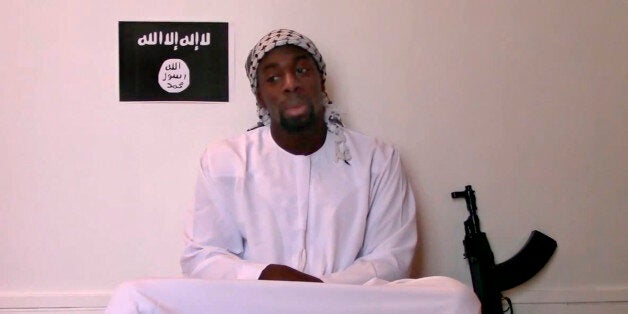 This image made from a video posted online by militants on Sunday, Jan. 11, 2015, shows slain hostage-taker Amedy Coulibaly, who shot a policewoman and four hostages at a kosher grocery in Paris, with a gun in front of an Islamic State emblem as he defends the Paris attacks carried out on the satirical newspaper, police and a Jewish store. At one point in the video, Coulibaly says Charlie Hebdo will be attacked "tomorrow" and that he and the (Said and Cherif Kouachi) brothers were coordinating. Speaking in broken Arabic, he gave his allegiance to the head of the Islamic State. (AP Photo/Militant Video)