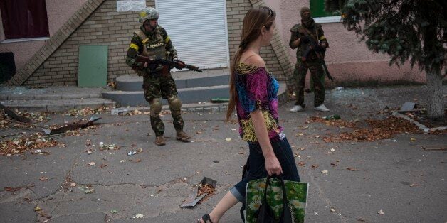 A woman walks past Ukrainian government soldiers from battalion "Donbass" guarding an entrance of a shop in village Mariinka near Donetsk, eastern Ukraine, Monday, Aug. 11, 2014. The Red Cross will lead an international humanitarian aid operation into Ukraineâs conflict-stricken province of Luhansk with assistance from Russia, the European Union and the United States, Ukraine said Monday.(AP Photo/Evgeniy Maloletka)