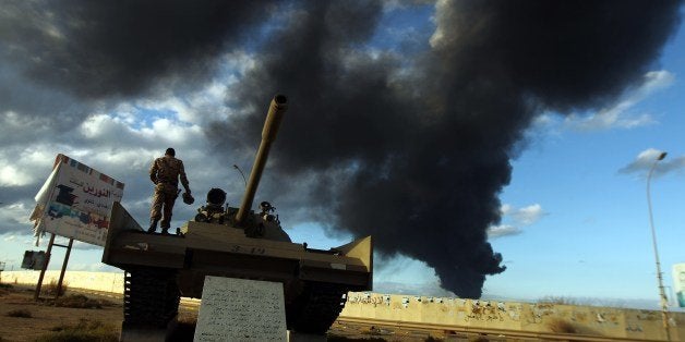 A member of the Libyan army stands on a tank as heavy black smoke rises from the city's port in the background after a fire b