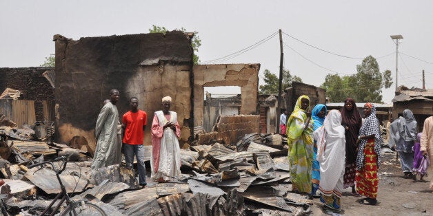 FILE- In this Sunday, May 11, 2014 file photo, people stand outside burnt houses following an attack by Islamic militants in Gambaru, Nigeria. Thousands of members of Nigeriaâs home-grown Islamic extremist Boko Haram group strike across the border in Cameroon, with coordinated attacks on border towns, a troop convoy and a major barracks. Further north, Boko Haram employs recruits from Chad to enforce its control in northeastern Nigerian towns and cities. In Niger, the government has declared a âhumanitarian crisisâ and appealed for international aid to help tens of thousands of Nigerian refugees driven from their homes by the insurgency. (AP Photo/Jossy Ola, File)