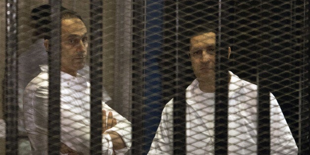 The sons of ousted Egyptian president Hosni Mubarak, Alaa (R) and Gamal are seen behind the defendants' cage during their retrial at the Police Academy in Cairo on June 8, 2013. All of the defendants have pleaded not guilty to the charges against them. AFP PHOTO / KHALED DESOUKI (Photo credit should read KHALED DESOUKI/AFP/Getty Images)