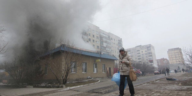 A woman resident passes by a burning house in Mariupol, Ukraine, Saturday, Jan. 24, 2015. A crowded open-air market in Ukrain