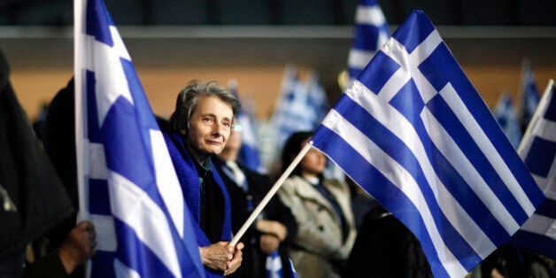 A supporter of the New Democracy party holds the Greek national flag during a pre-election rally by the party leader and Greek Prime Minister Antonis Samaras, not pictured, in Palaio Faliro, near Athens, Greece, on Friday, Jan. 23, 2015. Greek voters go to the polls on Jan. 25 in a general election that will decide whether Europe's most-indebted country sticks to an austerity program that ensures its financial lifeline from creditors such as Germany. Photographer: Kostas Tsironis/Bloomberg via Getty Images