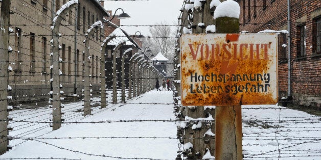 Visitors walk between barbed wire fences at the Auschwitz Nazi death camp in Oswiecim, Poland, Monday, Jan. 26, 2015. A decade ago, 1,500 Holocaust survivors traveled to Auschwitz to mark the 60th anniversary of the death camp's liberation. On Tuesday, for the 70th anniversary, organizers are expecting 300, the youngest in their 70s. Sign in foreground is an electric fence warning.(AP Photo/Alik Keplicz)