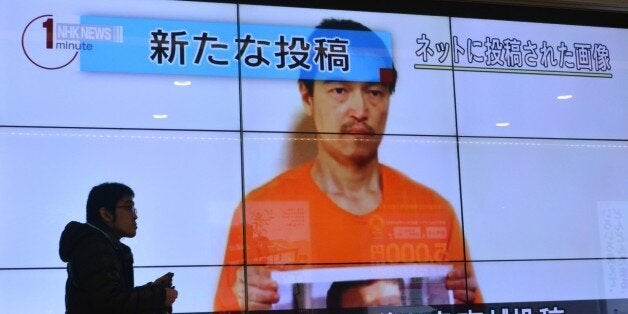 A pedestrian looks at a large screen in Tokyo on January 28, 2015 showing television news reports about Japanese hostage Kenj