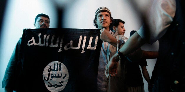 FILE - In this Tuesday, April 23, 2013 file photo, a suspected Yemeni al-Qaida militant, center, holds an Islamist banner as he stands behind bars during a court hearing in state security court in Sanaa, Yemen. Arabic on flag reads, "There is no God but Allah and Mohammed is the messenger of God." Al-Qaida in the Arabian Peninsula, suspected of having ties to the attackers in Paris, has been the most active of the terror network's branches in trying to strike in the West. (AP Photo/Hani Mohammed, File)