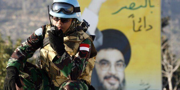 A peacekeeper of the United Nations Interim Force in Lebanon (UNIFIL) speaks on his talkie-walkie in front of a billboard bearing a portrait of Hezbollah chief Hassan Nasrallah during a patrol in the southern Lebanese town of Adaysseh, near the border with Israel, on January 19, 2015, one day after an Israeli air strike killed six Hezbollah members in the nearby Syrian-controlled side of the Golan Heights. Once solely focused on fighting the Jewish state, Shiite Hezbollah is now deeply involved in the war in neighbouring Syria, where it backs President Bashar al-Assad. AFP PHOTO / MAHMOUD ZAYYAT (Photo credit should read MAHMOUD ZAYYAT/AFP/Getty Images)
