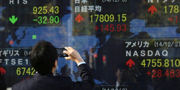 A man photographs an electronic stock board of a securities firm in Tokyo, Wednesday, Dec. 3, 2014. Japanese and Chinese sha