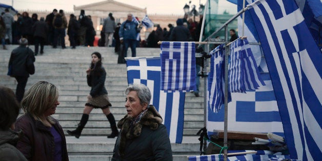 Women talk next to Greek flags for sale in Syntagma square, Monday, Feb. 16, 2015. Greece and its creditors in the 19-country eurozone struggled Monday to bridge a yawning gap over the country's request to ease its bailout terms despite a fast-approaching deadline. (AP Photo/Petros Giannakouris)