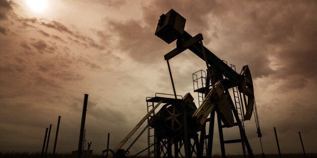 Operating oil and gas well silhouette in remote rural area, profiled on dramatic sky