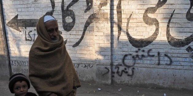 Pakistani pedestrians walk past wall graffiti (bottom) which reads Daesh, the arabic acronym for Islamic State (IS), in Pesha