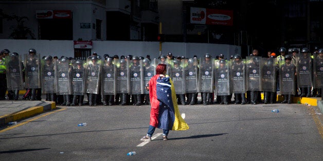 A demonstrator wearing a Venezuelan flag stands in front of police dressed in riot gear during a protest in Caracas, Venezuel