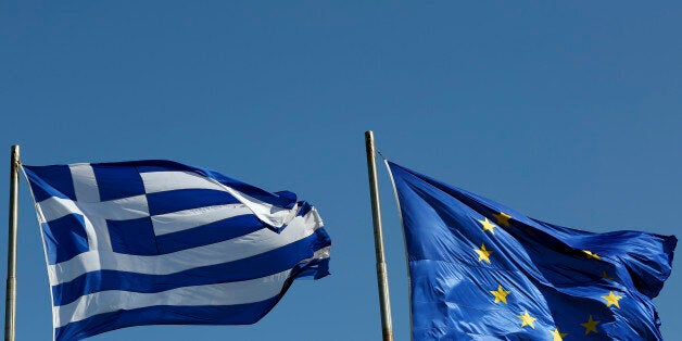 A Greek national flag, left, flies alongside a European Union (EU) flag in Athens, Greece, on Thursday, Feb. 19, 2015. Germany rebuffed Greece's request for an extension of its aid program, saying the Greek offer doesn't meet the euro region's conditions for continuing aid. Photographer: Kostas Tsironis/Bloomberg via Getty Images