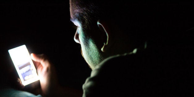 Man laying on bed at late night in a dark room checking his smartphone. Internet addiction.