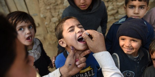 Pakistani polio vaccination worker Sher Khan (L) administers polio vaccine to a child in a poor neighbourhood that hosts Afghan refugees and internally displaced tribal people on the outskirts of Islamabad on December 29, 2014, during a vaccination campaign. Pakistan is one of only three countries where polio remains endemic. Attempts to stamp it out have been badly hit by opposition from militants and attacks on immunisation teams that have claimed 67 lives since December 2012. AFP PHOTO / Farooq NAEEM (Photo credit should read FAROOQ NAEEM/AFP/Getty Images)