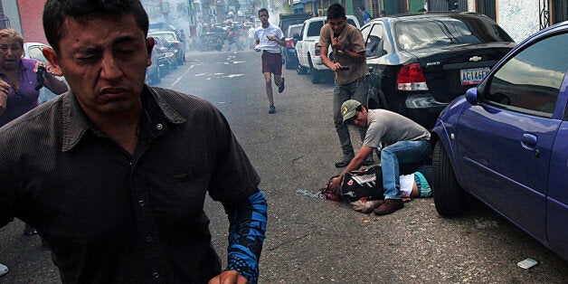 A man tries to help an injured youth lying on the ground in a pool of blood after he was shot in the head during an anti-government protest in San Cristobal, Venezuela, Tuesday, Feb. 24, 2015. Identified by Venezuela's Ombudsman as 14-year-old Kluiverth Roa, San Cristobal Human Rights Commission President Jose Vicente Garcia says preliminary investigations suggest the student was injured during a confrontation between protesters and police in the city, and died on the way to the hospital. (AP Photo)